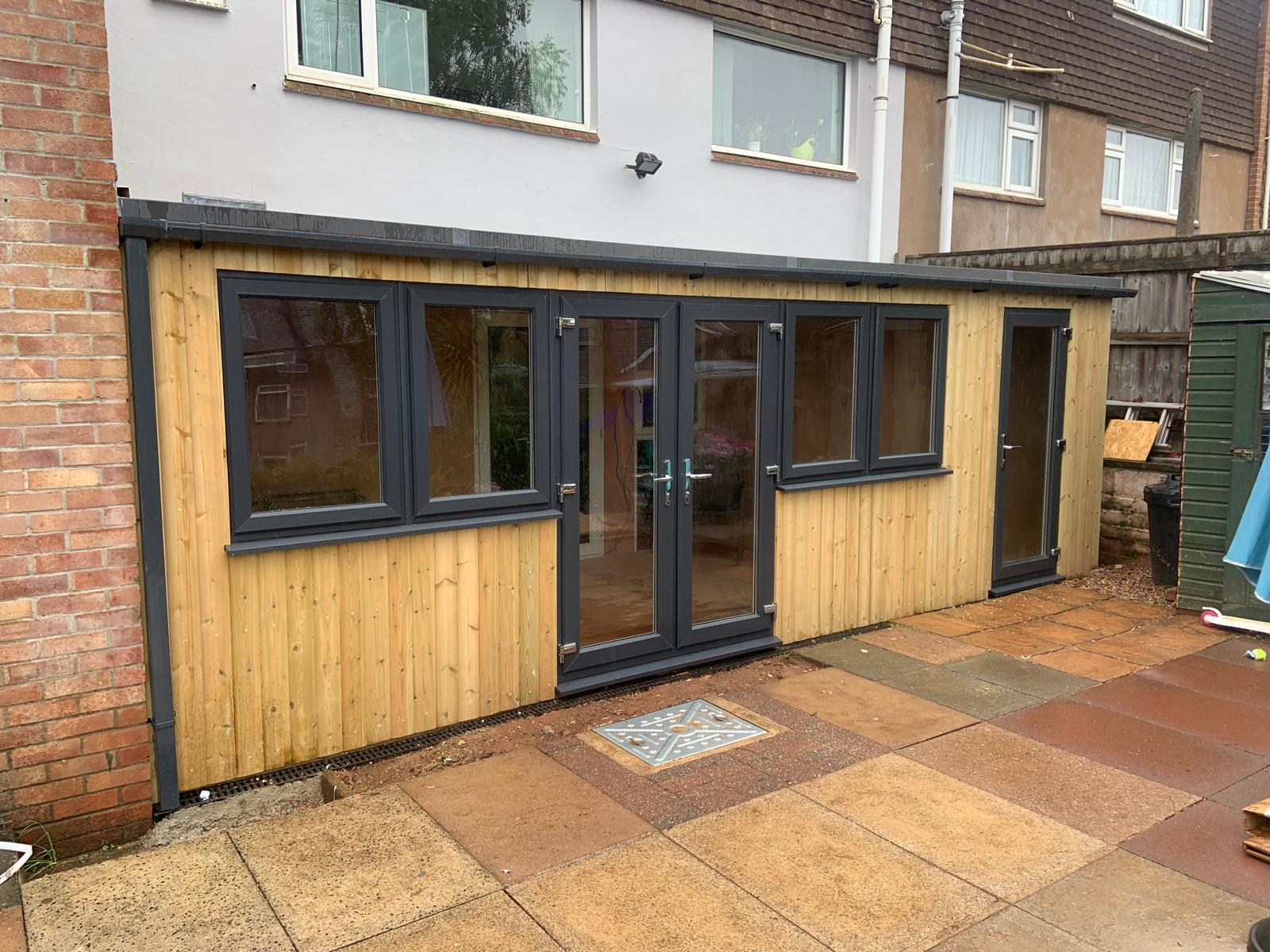 Timber Frame Extensions Timber clad single-storey extension with glazed doors on the back of a house